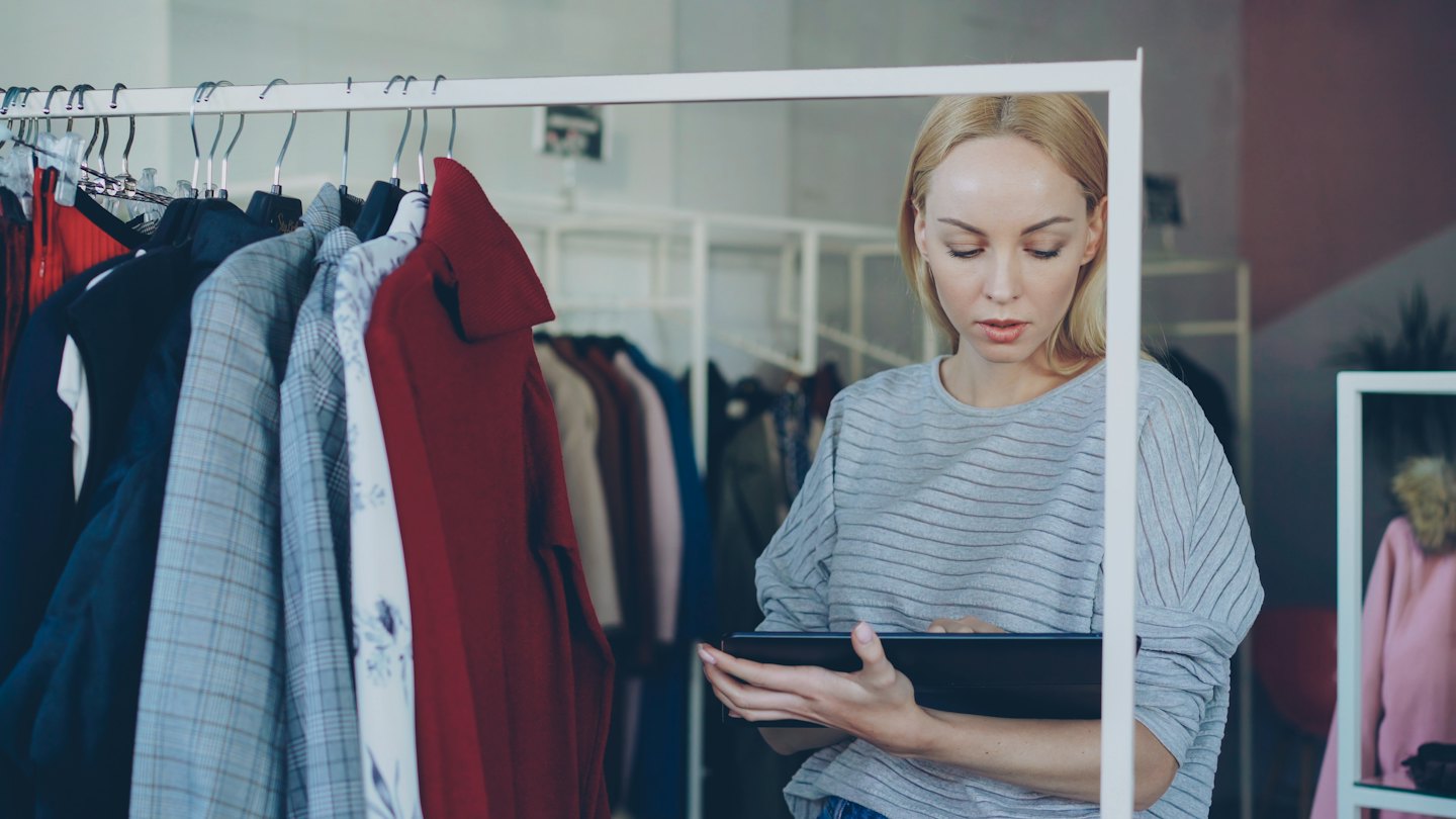 Professionista del retail usa un tablet per gestire l'inventario di una boutique di abbigliamento.